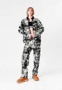 Conjunto de chaqueta y pantalones con un patrón abstracto en blanco y negro, que presenta un cuello y bolsillos, combinado con zapatos gruesos naranjas.