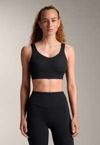 Črn športni modrček z širokimi naramnicami in U-izrezom, kombiniran z črnimi legicami visoke pasu. Gladka tekstura, minimalističen dizajn.