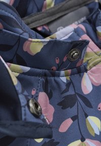 Tkanina w kwiatowy wzór w granatowym kolorze, z różowymi i żółtymi kwiatami. Zbliżenie ukazuje metalowy guzik z zatrzaskiem oraz szczegóły teksturowanego przeszycia.