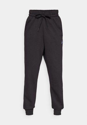 Pantalon de survêtement noir en tissu doux, avec une taille élastique et un cordon de serrage, et des jambes fuselées. Accent de logo subtil sur le côté.