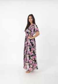 Robe maxi florale à manches courtes, en tissu noir avec de grandes fleurs roses et blanches, taille cintrée avec un lien, texture transparente.