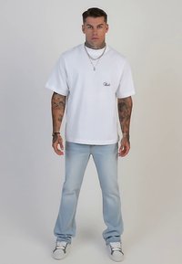 Camiseta blanca de algodón con mangas cortas y un pequeño logo, combinada con jeans de mezclilla azul claro y zapatillas blancas.