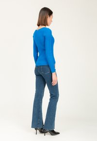 Blauw geribbelde lange mouwen top met een aansluitend ontwerp en achterkantdetail, gecombineerd met blauwe flared jeans en zwarte haklaarzen.