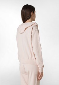 Sudadera con capucha de color rosa claro hecha de algodón suave, con puños y dobladillo acanalados, presentando un corte relajado y detalles de costura mínimos.