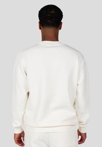 Sudadera blanca con canalé, cuello redondo, mangas largas y puños elásticos. Textura suave, corte relajado y sin patrones ni logotipos visibles.