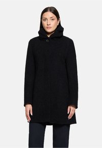 Zwarte wollen jas met een hoge kraag en een enkele knoopsluiting. Beschikt over een gestructureerd oppervlak en recht afgesneden mouwen.