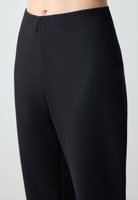 Pantalons noirs taille haute en tissu lisse, avec une coupe ajustée et un design minimaliste sans embellissements ni motifs.