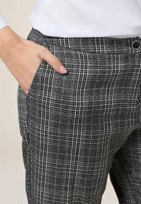 Grå och vit rutiga byxor med en avslappnad passform, med sidofickor och knappstängning. Tyget verkar texturerat och lätt.