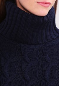 Dunkelblaues Rollkragensweatshirt aus dickem Strickmaterial mit einem Kabelmuster und geripptem Kragen. Nahaufnahme der Stoffstruktur.