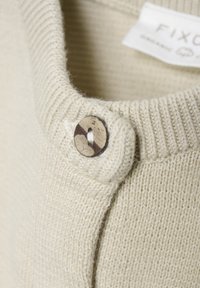 Ljust beige, stickad tröja med ribbat krage och en träknapp som accent på sidan. Mjuk textur med en enkel design.