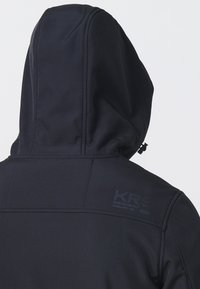Veste à capuche noire avec coutures visibles et un logo texte discret sur le haut du dos, à l'épaule droite.