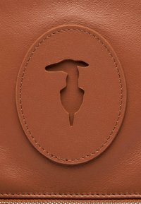 Bolso de cuero marrón con un diseño de corte circular. Textura suave con costuras visibles y cierre de cremallera. Sin detalles adicionales.