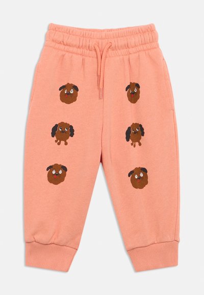 Pantalons de survêtement pour enfants couleur pêche avec taille élastique, cordon, poignets côtelés et visages de chiens dessinés marron imprimés sur les jambes avant.