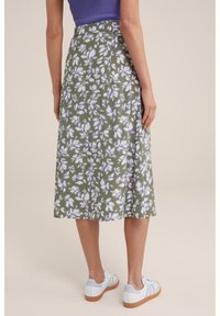 Kukallinen midi-hame vihreästä kankaasta, jossa on valkoisia ja vaaleanpurskeita lehtikuvioita. Hame on yhdistetty valkoisiin tennareihin, joissa on vaaleansinisiä yksityiskohtia ja kumipohjat.