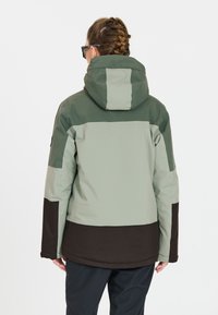 Waterdichte jas in lichtgroen en donkerbruin. Met een capuchon, een kleur geblokt ontwerp en een gladde textuur. Achteraanzicht weergegeven.