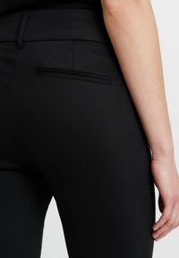 Czarne dopasowane spodnie o gładkiej fakturze, z tylną kieszenią z poziomym szwem. Zaprojektowane dla eleganckiego wyglądu.