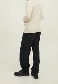 Svarta denimjeans med en avslappnad passform, matchat med en beige långärmad topp. Modellen har på sig svarta sneakers och står med ryggen mot kameran.