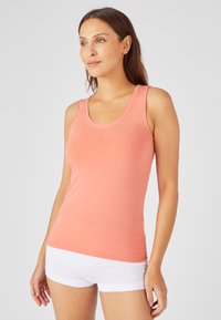Top senza maniche color pesca con scollatura rotonda e bordo ondulato. Realizzato in tessuto leggero, presenta una forma aderente.