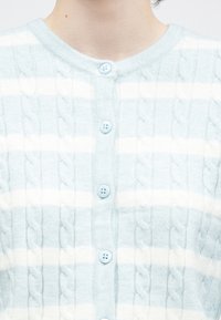 Světlomodrý kardigan s bílými pruhy, zdobený vzorem copánkového pletení, kulatým výstřihem a modrými knoflíky po celé přední straně.