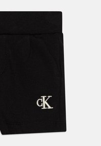 Černé bavlněné šortky s elastickým pasem, se bočními kapsami a bílým vyšitým logem "cK" na dolní levé straně.