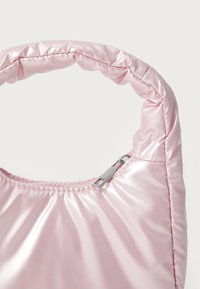 Sac en nylon rose, brillant, avec une texture matelassée et un léger éclat. Dispose d'une courte anse rembourrée et d'un détail de fermeture éclair en argent.