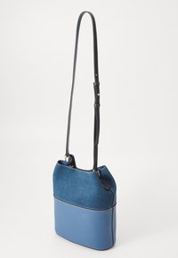 Blue bag with a suede upper and smooth lower section. Adjustable strap, rounded shape, and contrasting stitching detail on edges.