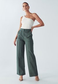 Jednoročný rebrovaný biely top v kombinácii s vysokým pásom, širokými zelenými nohavicami s prednými záhybmi. Hladká látka, topánky v neutrálnom odtieni.