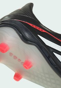 Μαύρο ποδοσφαιρικό παπούτσι με κόκκινες λεπτομέρειες και λευκές ρίγες. Διαθέτει υφή επιφάνειας και διάφανο πέλμα με τέσσερις κόκκινες τάπες.