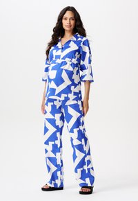 Blauw en witte outfit met een patroon, bestaande uit een knoopstructuur bovenstuk en wijde broek. De stof lijkt lichtgewicht met een losse pasvorm en opvallende vormen.