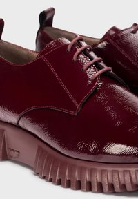 Zapatos de charol burdeos con un acabado brillante, que presentan una puntera redondeada, diseño con cordones y una suela de goma gruesa y estriada.