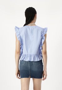 Blouse rayée bleue et blanche avec des épaules froncées, taille peplum et tissu doux. Associée à une mini-jupe en denim avec poches arrière.