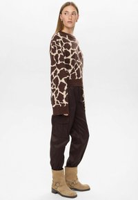 Pull à motif girafe brun et crème, coupe ample. Assorti avec un pantalon cargo noir et des bottines beige à détail de boucle.