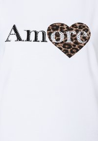 White t-shirt featuring the word "Amore" in black and silver rhinestones, with a leopard print heart accenting the "o."