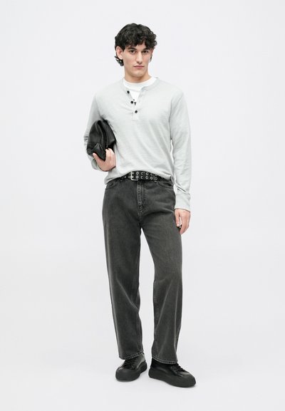 Šviesiai pilkas ilgomis rankovėmis henley stiliaus marškinėliai su trimis mygtukais, derinami su tamsiai pilkomis tiesaus silueto džinsais ir juodais sportbačiais. Rankose laikoma juoda rankinė.