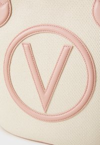 Bežinė tekstūruota rankinė, kurioje yra didelis iškilus rožinis "V" logotipas su apvaliu rožiniu kontūru. Lygūs odos akcentai pagerina jos dizainą.