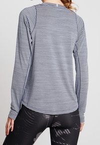 Koszula z długim rękawem w granatowo-białe paski, wykonana z lekkiego materiału. Posiada zaokrąglony dekolt oraz kontrastowe szwy.