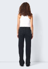 Sorte denimjeans med rette ben, som har to baklommer og høy midje, kombinert med en hvit ribbet tank topp.