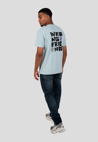 Vaaleansininen t-paita, jossa on "WRONG FRIENDS" -teksti mustana ja värikkäitä luurankokuvastoja selässä. Pehmeää kangasta, lyhyet hihat.