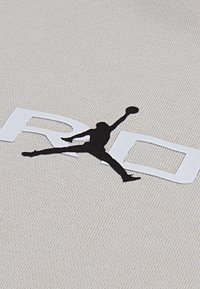 Tessuto beige chiaro con una superficie texture che presenta un logo bianco con la "R" e la "D". Silhouette nera di una figura che salta mentre tiene in mano una palla.