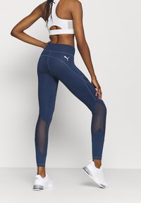 Navy leggings with mesh accents, featuring a high waistband and contrasting seam lines. Pairing with white athletic shoes.