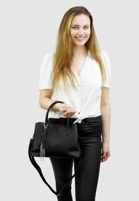 Zwarte handtas met textuur, ronde bovenhandvaten en een afneembare schouderriem, voorzien van een decoratieve kwast en kettingaccenten.