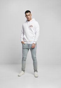 Hvit hettegenser med rød grafisk tekst, frontlomme, kombinert med lyseblå skinny jeans og hvite joggesko.