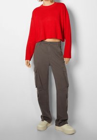 Roter, kurz geschnittener Pullover mit langen Ärmeln, kombiniert mit grauen Cargo-Hosen mit Seitentaschen und beigen Plateausneakern.