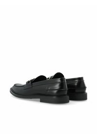 Mocasines de cuero negro con un diseño elegante, que presentan un acento plateado, puntera redonda y suela plana de goma. Textura suave con detalles de costura.