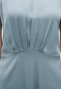 Gros plan d'une robe bleu clair avec des plis verticaux sous la poitrine et une ceinture lisse.