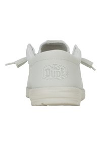 Zapatillas slip-on blancas de lienzo con textura suave, suela de goma y lengüetas traseras dobles para facilitar su uso. Presentan el logo en relieve "HEY DUDE".