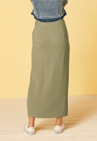 Olijfgroene maxi rok met een gladde textuur en een rechte silhout, voorzien van een tailleband en gecombineerd met witte sneakers.