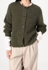 Zielonooliwkowy kardigan z dzianiny z okrągłym dekoltem, luźnym krojem i pięcioma ciemnymi guzikami z przodu. Teksturowana tkanina z prążkowanymi rękawami.