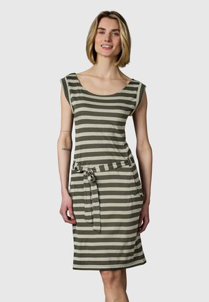 Frau steht und lächelt, trägt ein ärmelloses knielanges Kleid mit horizontalen grauen und weißen Streifen und einen gebundenen Stoffgürtel.