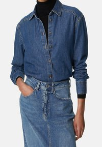 Denimskjorta i blått, med knäppning fram, långa ärmar och kontrasterande sömmar. Kombinerad med en matchande denimkjol.